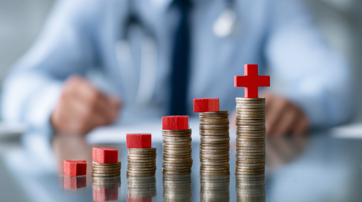 Stacks of coins with red blocks on top, symbolizing rising healthcare and insurance costs