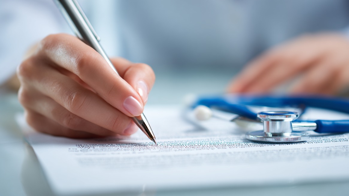 Hand signing insurance document with a stethoscope beside it
