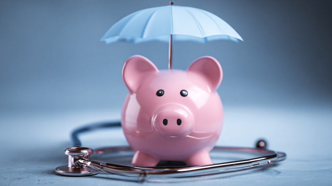 Pink piggy bank under a small blue umbrella with a stethoscope wrapped around it, symbolizing insurance protection