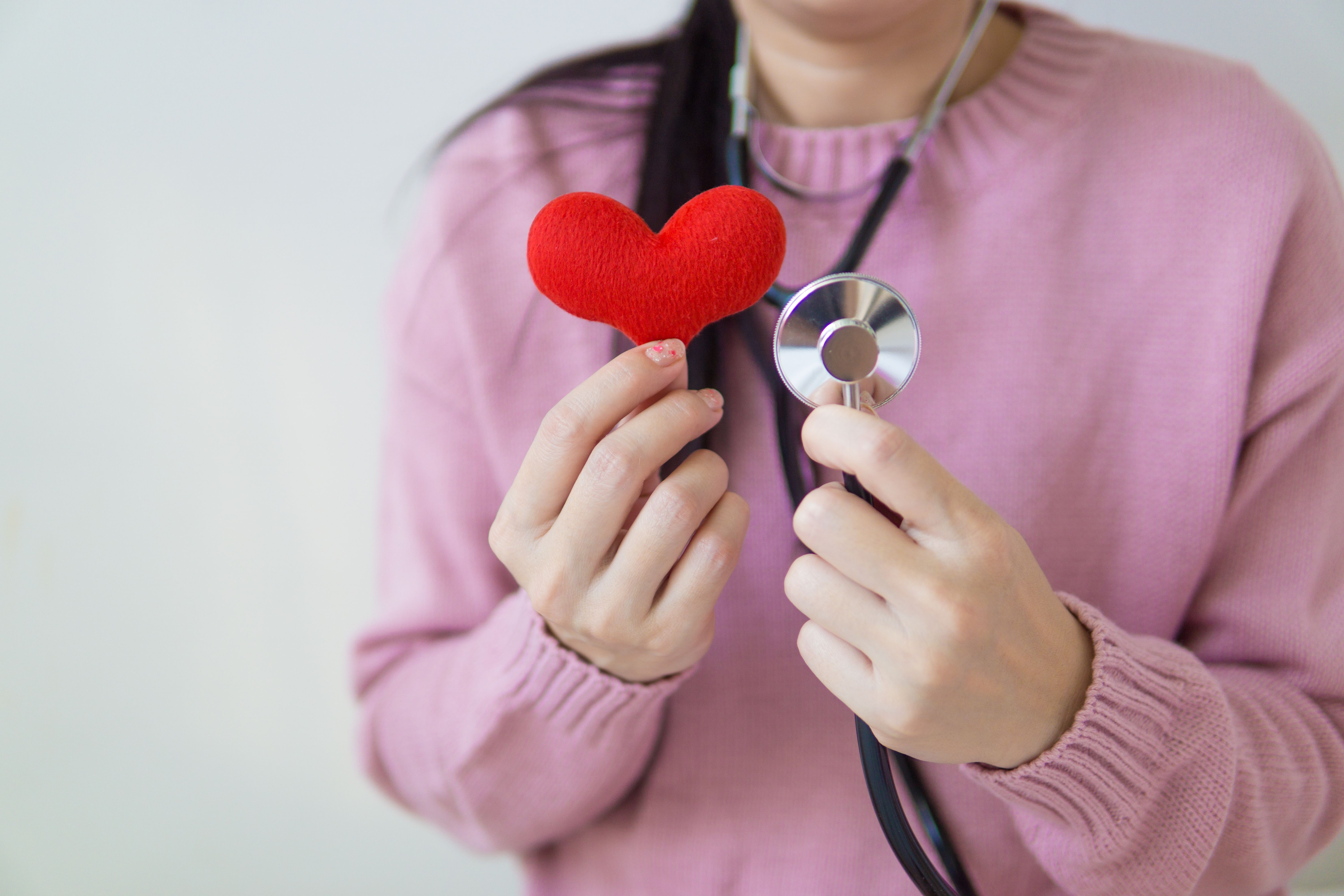 Person in medical attire holding a red heart model symbolizing heart health